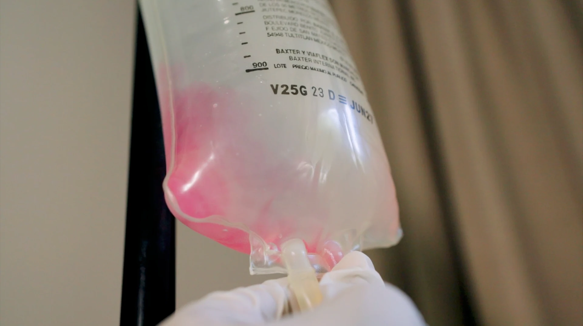 Bolsa de infusión intravenosa sostenida por una mano con guante.